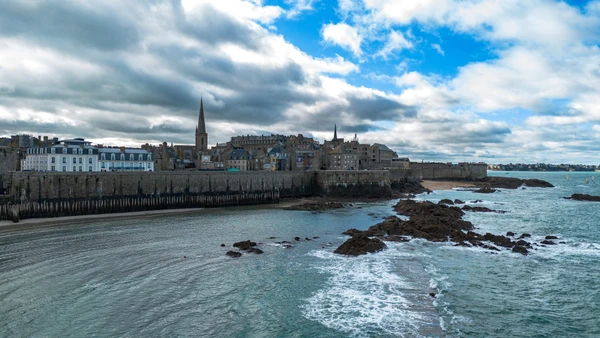 Vue pittoresque des remparts fortifiés de Saint-Malo en Bretagne, photographiée de jour avec un ciel partiellement nuageux. Au premier plan, on voit les caractéristiques murailles historiques de la cité corsaire. La photo capture l'architecture défensive bretonne typique et l'atmosphère côtière de la région, sans texte, logo ou filigrane. Cette image contextualise visuellement la présence locale de l'entreprise sur la Côte d'Émeraude.