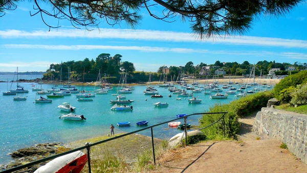 Photographie en couleur d'une vue caractéristique de Saint-Briac-sur-Mer en Bretagne : paysage côtier avec plage de sable, falaises côtières et rochers granitiques typiques de la Côte d'Émeraude. La scène capture l'essence bretonne du littoral nord avec ses formations géologiques distinctives, prise de jour avec une bonne luminosité naturelle. Sans texte, logo ou filigrane.